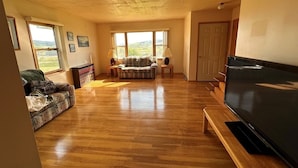 A spacious living room with hardwood floors, a large flat-screen TV, a sofa, and a coffee table.
