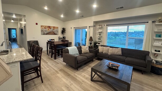 A spacious living room with a dining area, a kitchen with granite countertops, and a large window offering a view of the city.