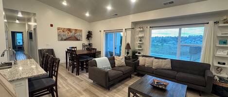 A spacious living room with a dining area, a kitchen with granite countertops, and a large window offering a view of the city.