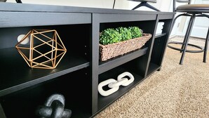 Un bureau noir doté de compartiments de rangement géométriques et en forme de chaîne, un panier tressé contenant des plantes vertes, et une chaise à l’arrière-plan.