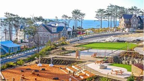 Een woongebied aan de kust met huizen, een verharde voetpad en uitzicht op de oceaan.