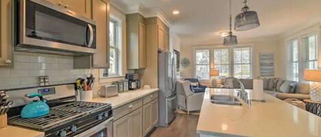 A modern kitchen with a large stove, microwave, and refrigerator. There is a dining area with a table and chairs, and a living room with a sofa and a coffee table.
