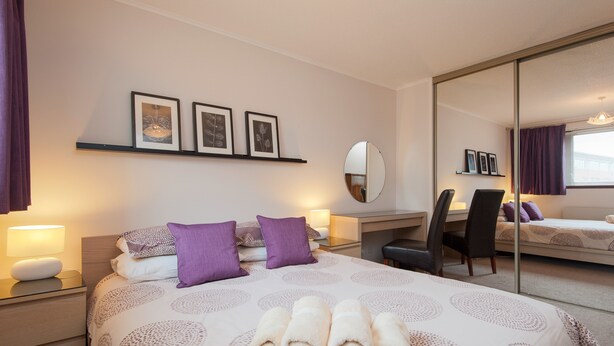 A hotel room with a bed, a desk, a chair, a mirror, and a shelf with pictures. - A modern 2-bedroom apartment in a quiet neighbourhood . Sleeps 4 (Edinburgh)