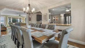 A dining area with a large wooden table, grey upholstered chairs, and a chandelier. - Lakefront Retreat on Intermediate Lake | Sleeps 14 • Firepit Dogs (Central Lake)