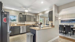 A modern kitchen with granite countertops, stainless steel appliances, and a dining area with a large island and chairs. - Lakefront Retreat on Intermediate Lake | Sleeps 14 • Firepit Dogs (Central Lake)