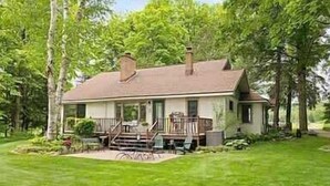 A single-story house with a porch, surrounded by trees and a well-maintained lawn. - Lakefront Retreat on Intermediate Lake | Sleeps 14 • Firepit Dogs (Central Lake)
