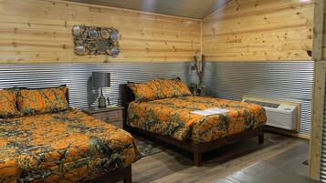 Een kamer met twee houten bedden, een hoofdeinde van metaal, een wandheater en een klein tafeltje met een lamp.