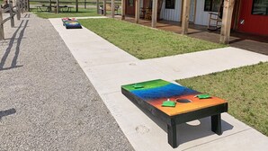 Un espace extérieur aménagé en bois avec des tables et des chaises, un espace de pique-nique couvert et un bâtiment à la façade rouge.