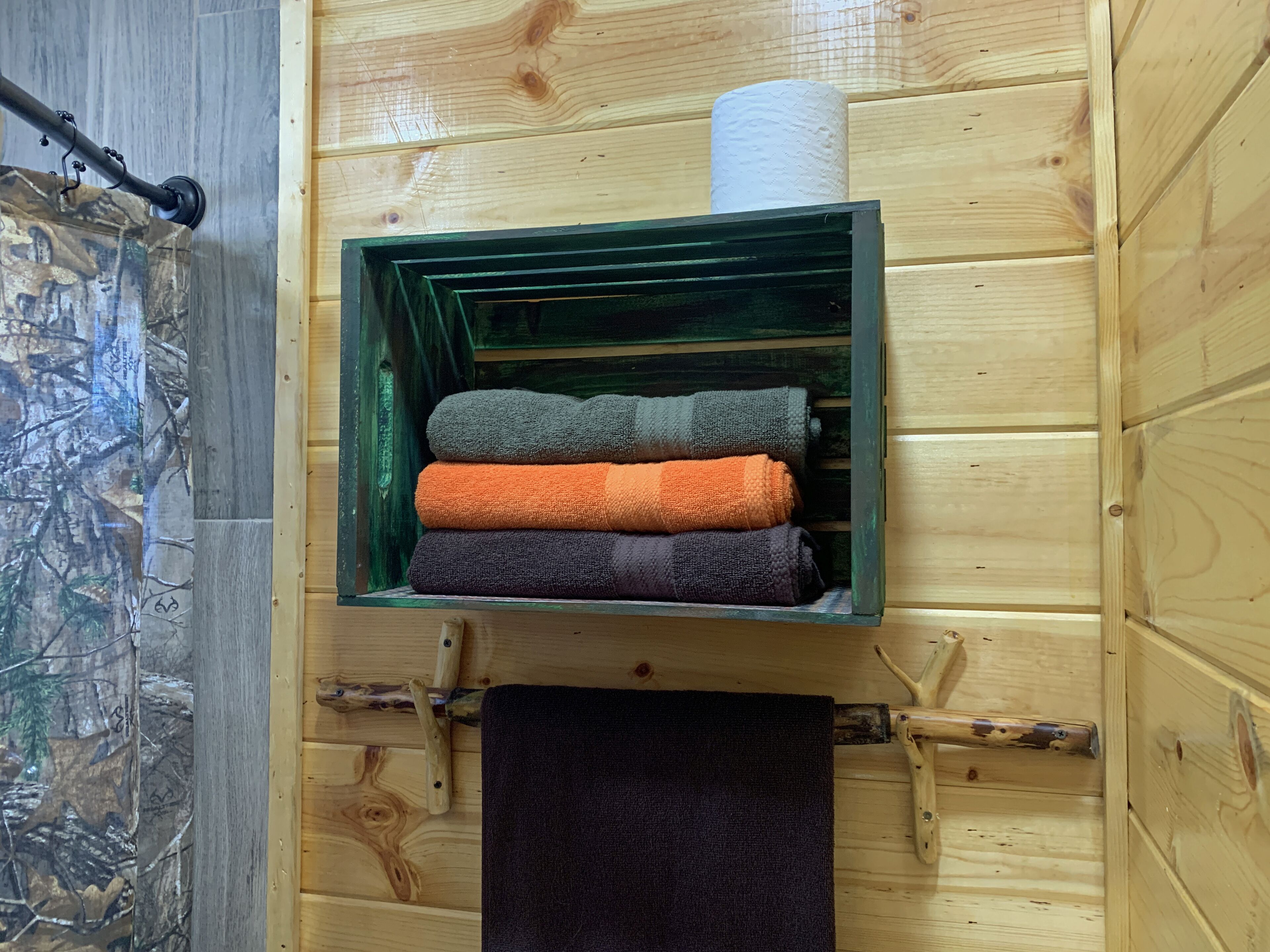Een houten muur met een plank waarop opgevouwen handdoeken in groen, oranje en paars liggen.
