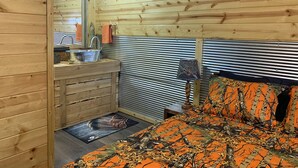 L'intérieur d'une cabane en bois, avec un lit, un lavabo et un miroir.