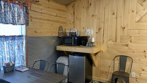 Une cuisine compacte aux murs en bois, avec une table à manger, des chaises, un réfrigérateur, un four à micro-ondes et une machine à café.