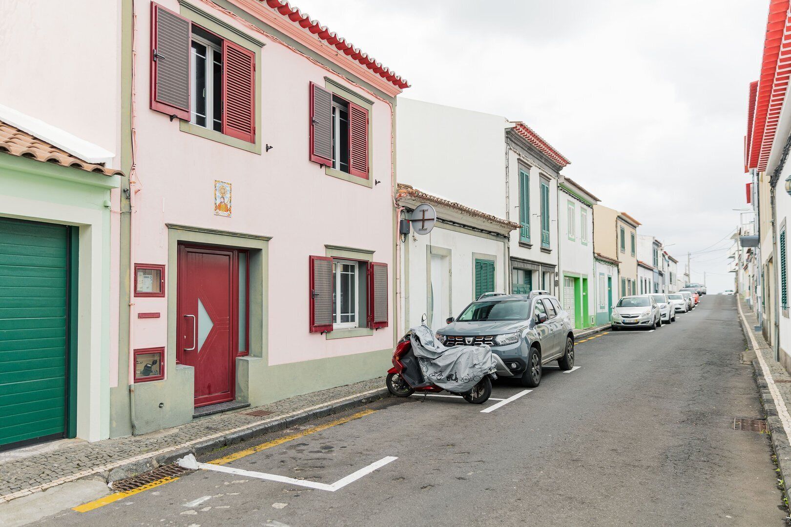 A narrow street lined with colorful buildings, parked cars, and a motorcycle.