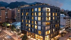 Un hôtel moderne à plusieurs étages, situé à un carrefour, doté d’un vaste espace extérieur aménagé avec des sièges et offrant une vue sur le paysage urbain environnant.