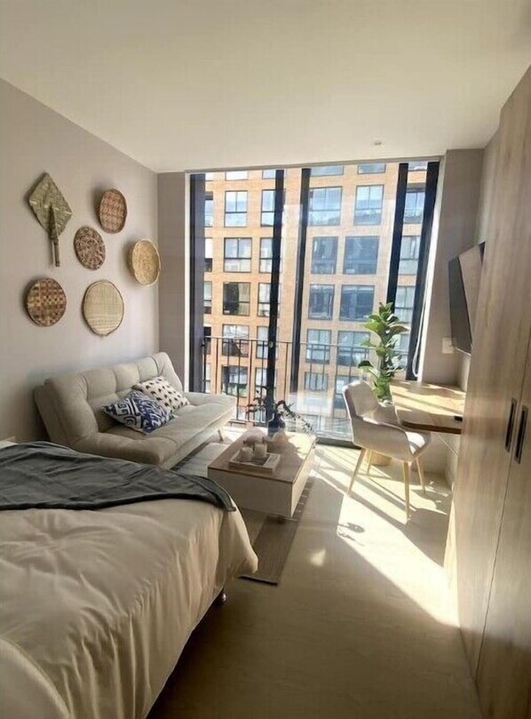 A modern bedroom with a bed, a sofa, a desk, and a large window with a city view. - Chic Zona Rosa Loft · Rooftop & Coworking (Bogotá)
