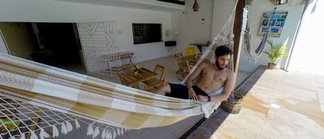 Una hamaca en una habitación con suelo de baldosas, muebles de madera y techo con vigas a la vista.