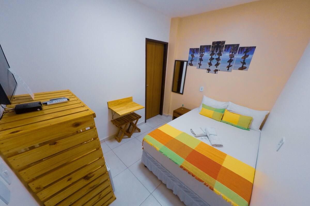 A bedroom with a bed, wooden dresser, desk, and a wall-mounted artwork.
