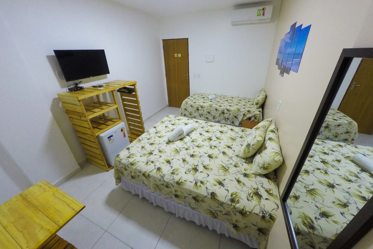 A bedroom with a bed, a TV, a wooden shelf, and a mirror.