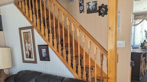 Una sala de estar con sofá de cuero negro, escalera de madera y una obra de arte colgada en la pared.