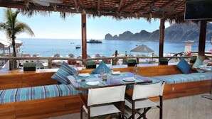 A beachside restaurant with wooden furniture, a thatched roof, and a view of the sea and mountains. - Beach Access!! Beautiful Oceanfront Resort! Room upgrades available!  (Cabo San Lucas)