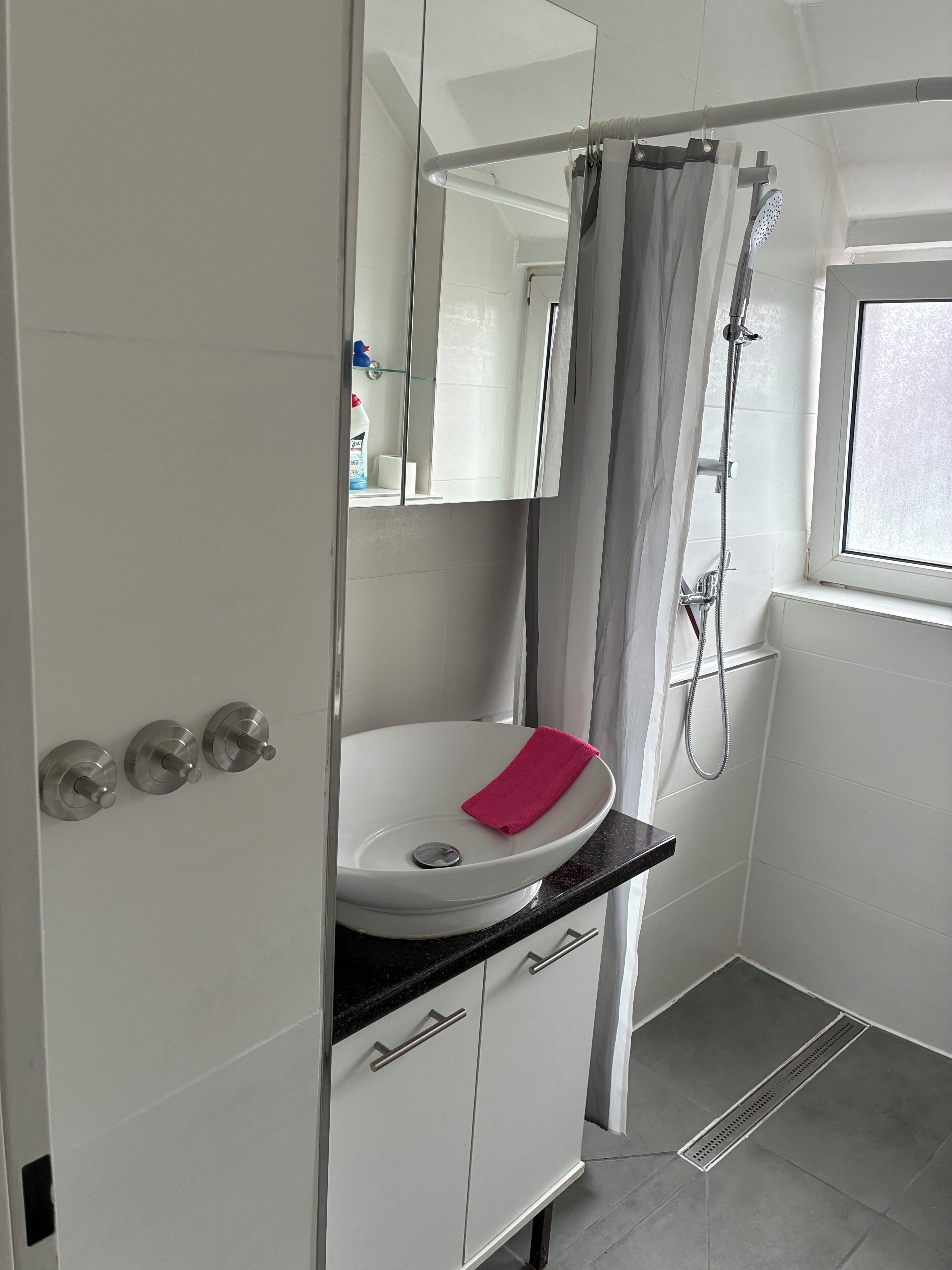 Ein Badezimmer mit Waschbecken, Dusche, Fenster und Spiegel.