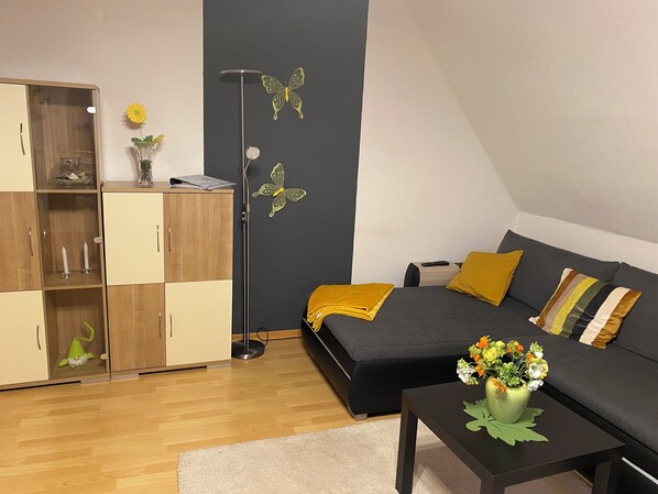 A modern living room with a dark grey sofa, yellow cushions, a black coffee table with a vase of flowers, a wooden wardrobe, and a floor lamp with butterfly wall decorations. - Sonnenschein House 2 (Lage Lippe)