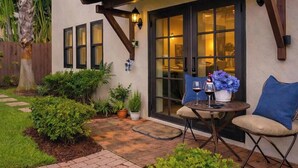 Un patio con una mesa, sillas, una planta en maceta y una botella de vino.