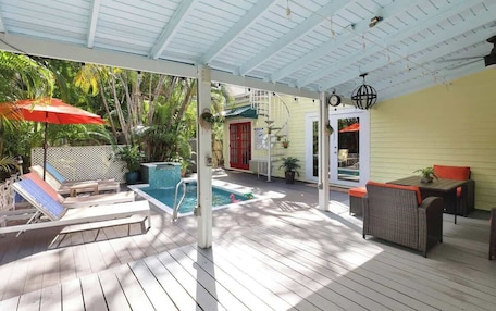 A covered outdoor area with a pool, lounge chairs, and wicker furniture.