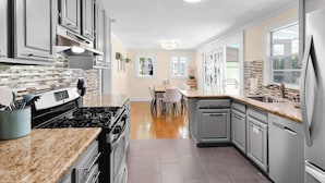 Uma cozinha moderna com bancadas de granito, eletrodomésticos de aço inoxidável e uma área de jantar com mesa e cadeiras de madeira.