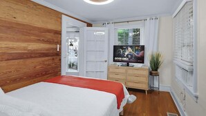 Quarto com cama, televisão, guarda-roupa de madeira e janela com cortinas.