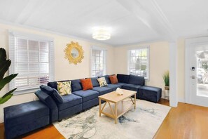 A living room with a sectional sofa, a coffee table, and a sunburst mirror on the wall.