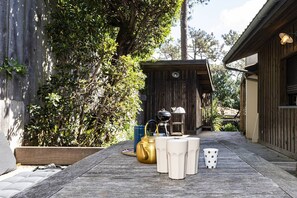 A wooden deck with a rustic outdoor seating area, a small wooden structure, and a garden wall. - Belle villa en plein coeur du Cap-Ferret à quelques pas des plages (CAP FERRET)