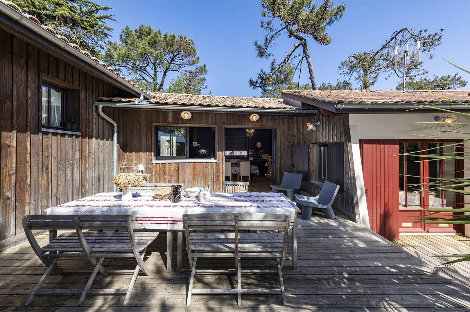 Une terrasse en bois avec une table et des chaises, un petit coin cuisine et une porte rouge.