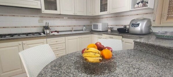 A kitchen with white cabinets, a granite countertop, a microwave, a toaster, and a fruit bowl with bananas and oranges. - Appartamento con Piscina per 6 Persone (Caltanissetta)