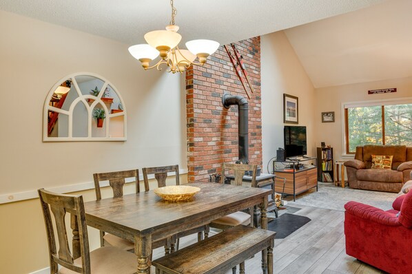 A dining area with a wooden table and chairs, a chandelier, and a brick wall with a chimney. - Spacious Bartlett Condo w/ Balconies & Pool! (Bartlett)