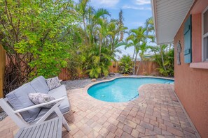 Un jardin avec une piscine, une terrasse en bois et un canapé d’extérieur blanc.