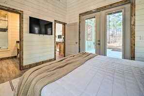 A bedroom with a large bed, a television mounted on the wall, and a sliding glass door leading to an outdoor area.