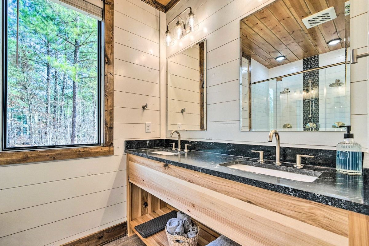 Un baño con un ventanal grande, paneles de madera, encimera de mármol y espejo con zona de ducha.
