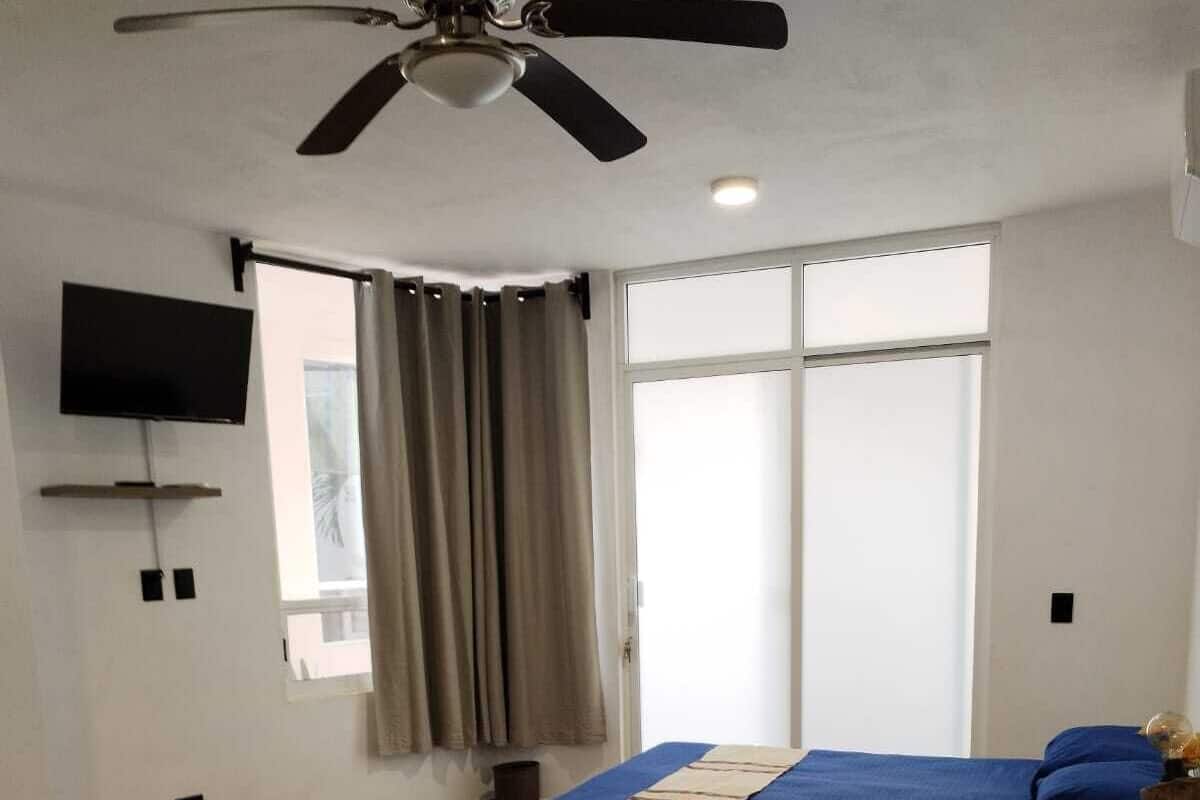 Een hotelkamer met twee bedden, een plafondventilator, een televisie en een raam met gordijnen.