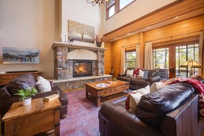 A cozy living room with a stone fireplace, leather sofas, and a large window offering a view of the outdoors. - Secluded Private Mountain Meadows | Hot Tub | Colorado Lodge (Tabernash)