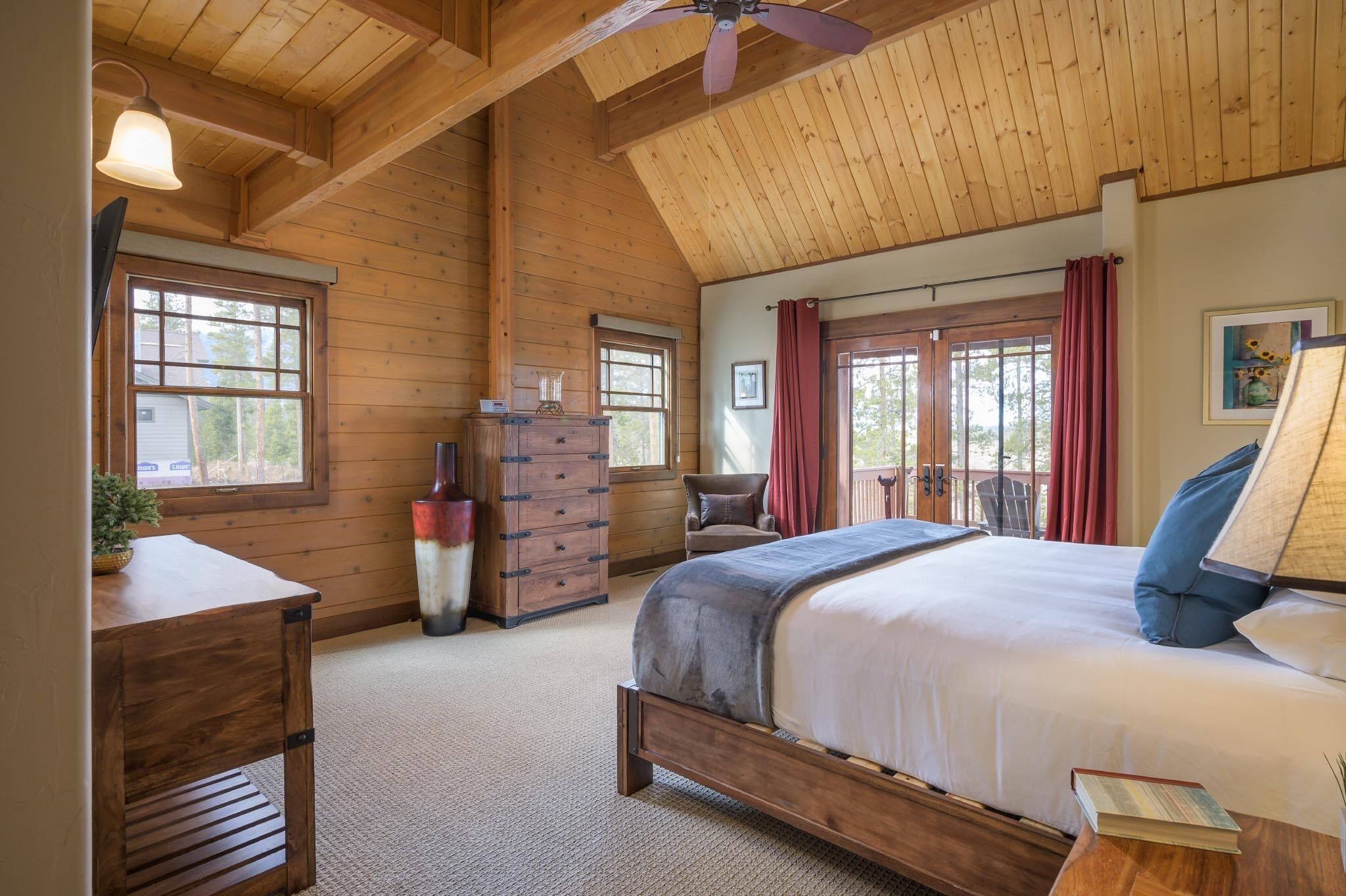 A wooden cabin bedroom with a bed, dresser, and windows.