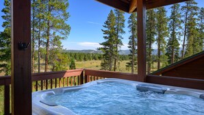 Ein Whirlpool auf einer Holzterrasse mit Blick auf Wald und Berge.