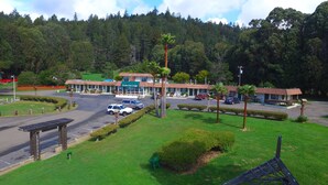 Un motel llamado Ocean Cove Lodge con un estacionamiento, varios coches y un césped verde con un banco.