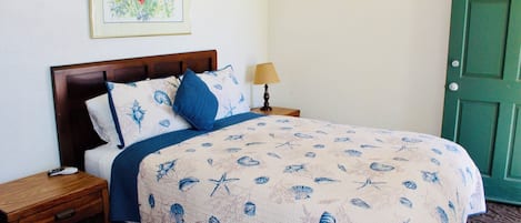 A neatly made bed with a floral print bedspread, a wooden nightstand with a lamp, and a green door.
