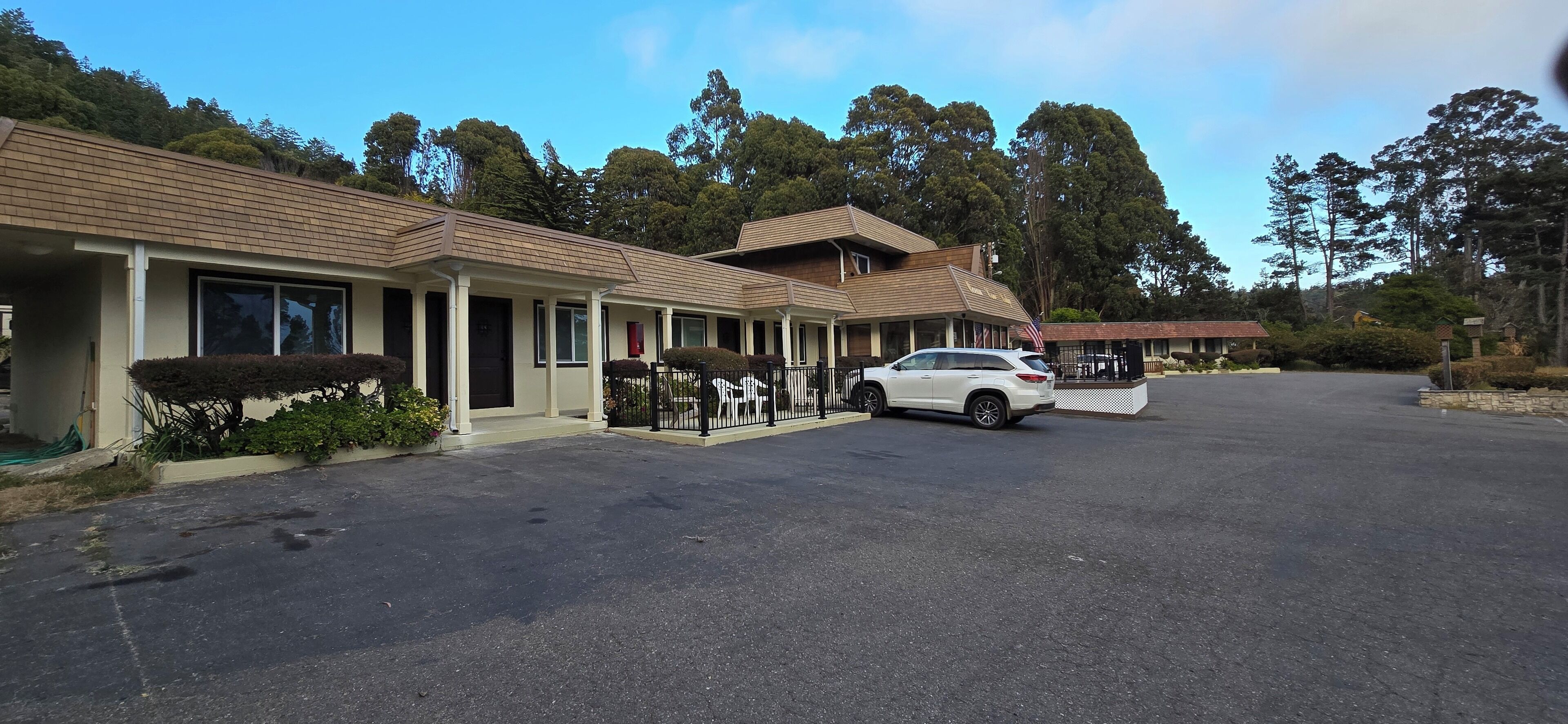 A motel with a parking lot, a white car parked in front, and a large tree in the background.