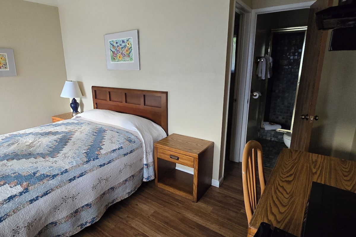 A bedroom with a wooden bed, a nightstand, a chair, and a door leading to a bathroom.