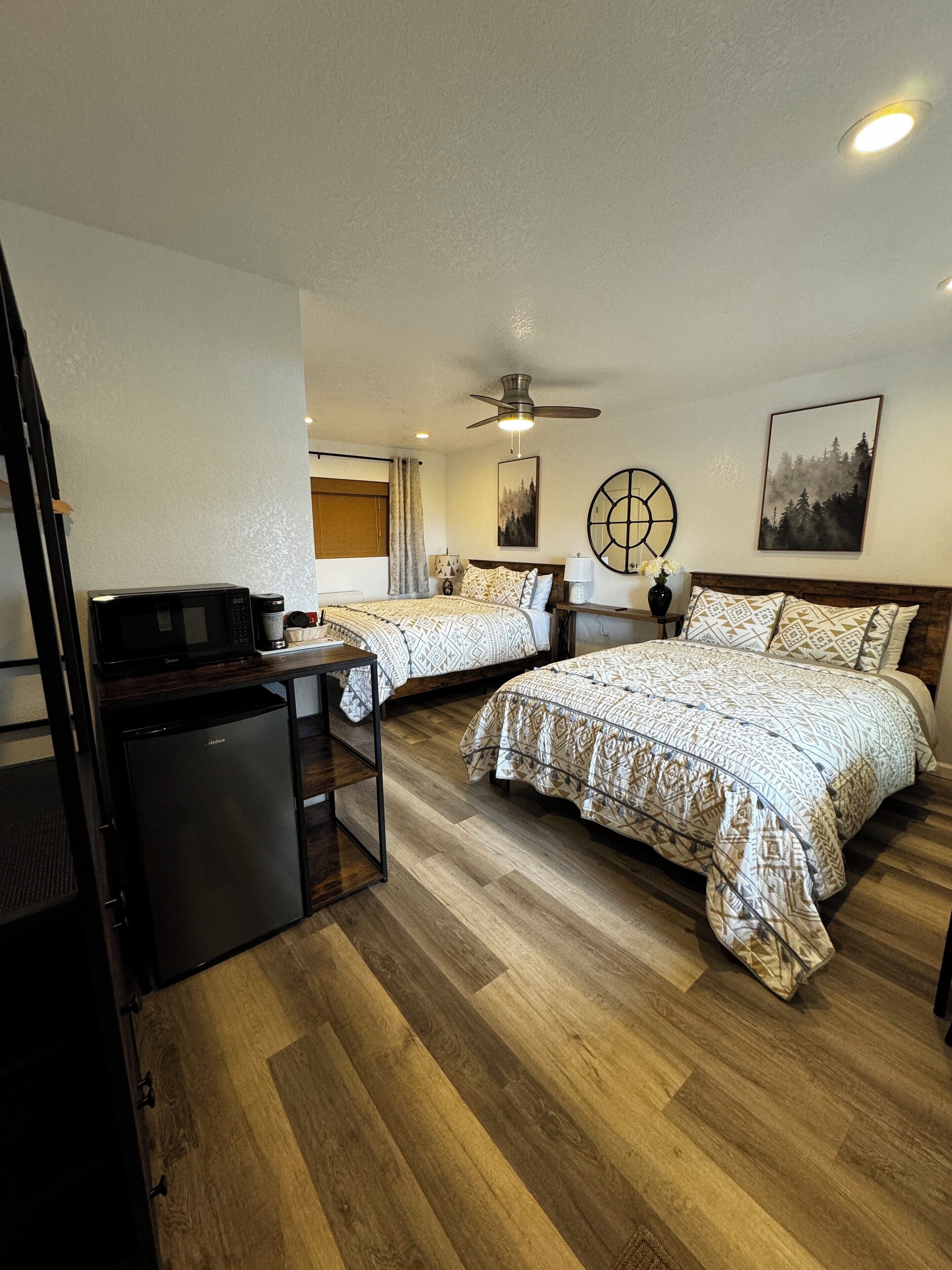 Een hotelkamer met twee bedden, een bureau, een koelkast, een plafondventilator en kunstwerken aan de muur.