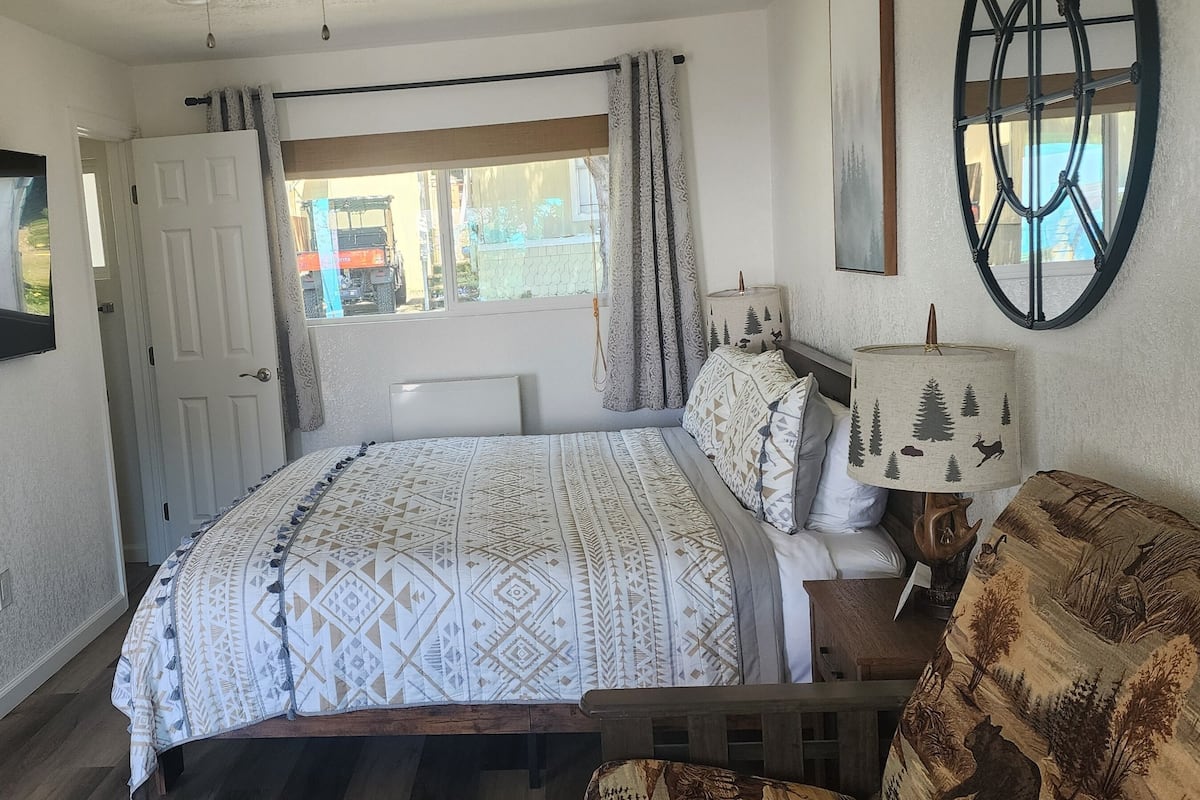 A bedroom with a bed, a window, a door, a mirror, and a lamp.