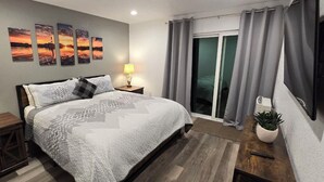 Un dormitorio moderno con una cama grande, dos lámparas de noche, un televisor de pantalla plana y un ventanal corredero a un balcón.
