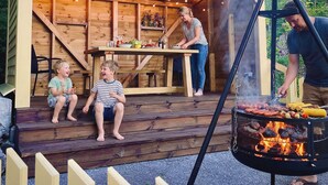 Eine Holzterrasse mit einem Grill, einem Tisch gedeckt mit Speisen und zwei Kindern, die auf Stufen sitzen.