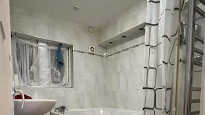 Une salle de bain moderne avec un lavabo, des toilettes et une baignoire blancs. On y trouve un rideau de douche et un tapis à motifs rouges sur le sol.